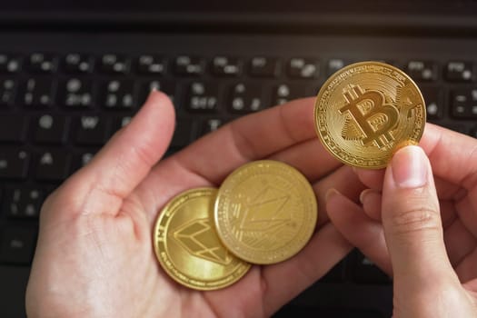 Woman hand holding golden coloured bitcoin and eos crytpocurrency coins over black laptop keyboard