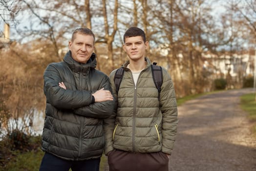 Father-Son Bond: Handsome 40-Year-Old Man and 17-Year-Old Son Standing Together in Winter or Autumn Park. Capture the essence of familial connection with this heartwarming image featuring a handsome 40-year-old man and his 17-year-old son standing side by side in a serene park. Whether embraced by winter's chill or adorned with autumn hues, it's a timeless snapshot of the enduring bond between father and son.