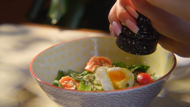 Close-up of woman adding spices to salad. Stock footage. Woman pepper salad with egg. Hearty seasoned salad or bowl with beautiful serving.