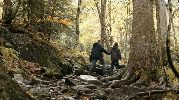 Young active woman and her son hiking, trekking in the woods. Creative. Autumn walk on stony path with tree roots