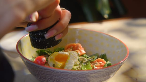 Close-up of woman adding spices to salad. Stock footage. Woman pepper salad with egg. Hearty seasoned salad or bowl with beautiful serving.