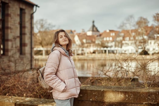 Young beautiful pretty tourist girl in warm hat and coat with backpack walking at cold autumn in Europe city enjoying her travel in Zurich Switzerland. Outdoor portrait of young tourist woman enjoying sightseeing