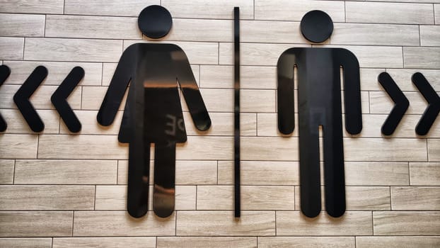 Male and Female Restroom Symbols on Wooden Wall With Directional Arrows. Gender-specific bathroom signs on wood surface