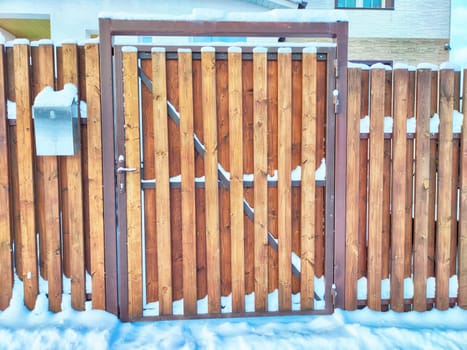 New gate, entrance to a private territory on a winter day and snow. Wooden texture and background. Fence