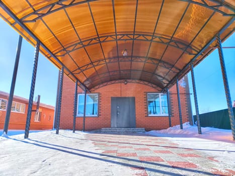 Wintertime at a Red Brick Building With Covered Entrance. Snowy landscape outside a brick structure under a clear sky
