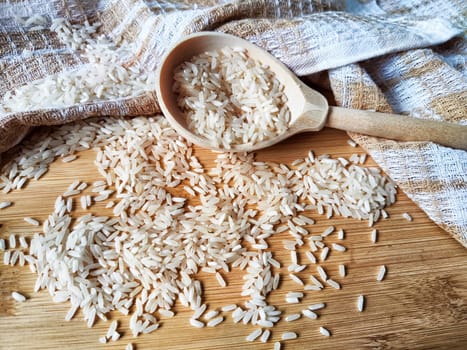 Rice scattered on textured fabric and in wooden spoon. Grits for cooking. Texture, background, copy space and place for text