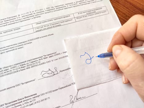 Hand hand of woman with pen meticulously tries to copy a signature from document. Violation of the law. Illegal signature