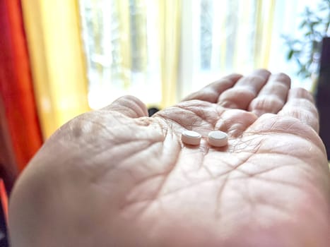 Close-up of an adult hand holding two small white pills. Close-Up of Two Pills in an Open woman Palm near window. Suicide. The choice of life or death