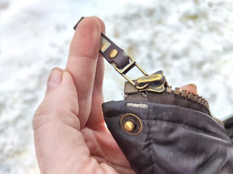 Fixing a broken zipper on a coat in woman hand outdoors during winter or spring