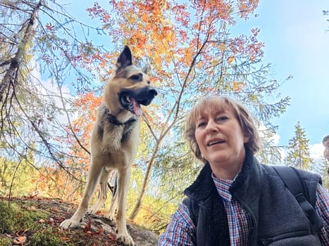 Adult girl with shepherd dog taking selfies in forest. Middle aged woman and big shepherd dog on nature. Friendship, love, communication, fun, hugs