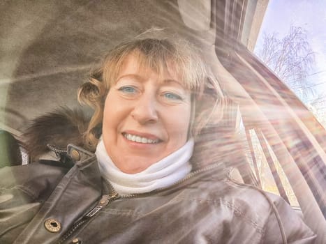 A woman in a car taking a selfie while enjoying a drive. Female driver posing inside car and the rays of the sun in the background