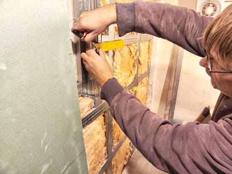 Professional Installs Drywall During Home Renovation. A skilled worker measures and secures drywall in a home under renovation