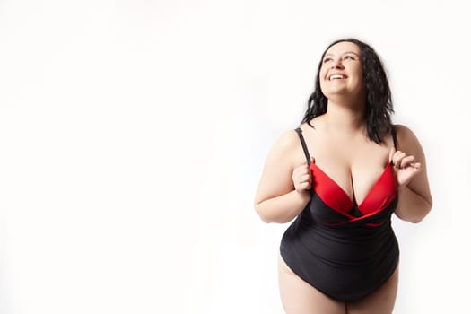 Portrait of attractive dreamy thick woman in red black swimsuit posing on white background. Body positive, photoshoot, selfie. Funny plus size model