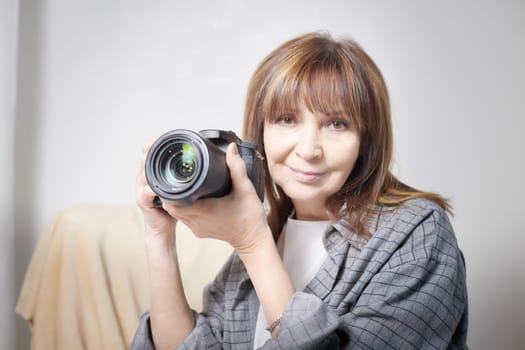 Senior old elderly woman with black camera with a large lens indoors in the studio. Professional photographer. Age Hobby