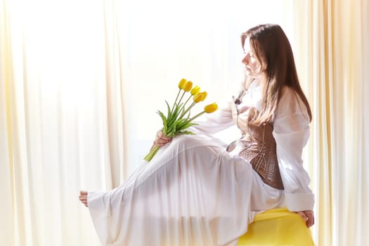 Beautiful sweet girl in nightgown in early morning with bouquet of delicate yellow tulips. Gift on International Women's Day on March 8th. Cosmetics, skin and hair care. Perfume, natural fragrance