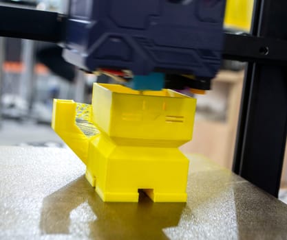 3D printer prints object. Process of printing yellow model on 3D printer. Model printed on 3D printer from molten plastic. 3D printing technologies. Additive progressive new modern printing technology