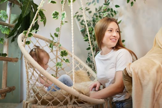 Happy loving family. Mother and daughter child girl playing and hugging in living room with wicker chair