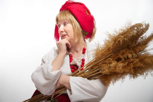 Portrait of heerful funny adult mature woman solokha with sheaf of ears. Female model in national ethnic Slavic style. Stylized Ukrainian, Belarusian or Russian woman in comic photo shoot