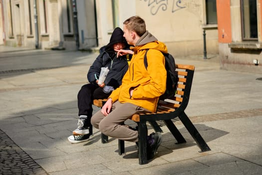 A teenage boy and a teenage girl are sitting on a bench