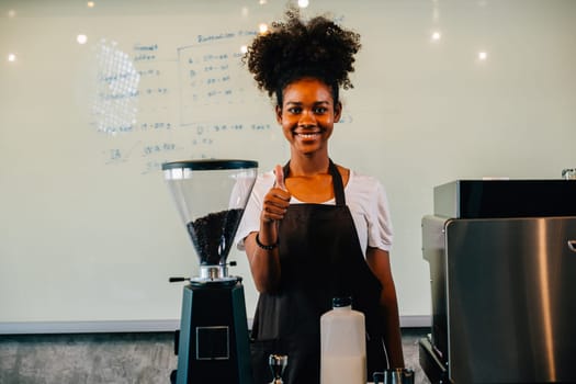 At the cafe a confident black woman stands at the counter. Portrait of owner a successful businesswoman in uniform smiling with satisfaction ensuring customer service. Inside a small business cafe