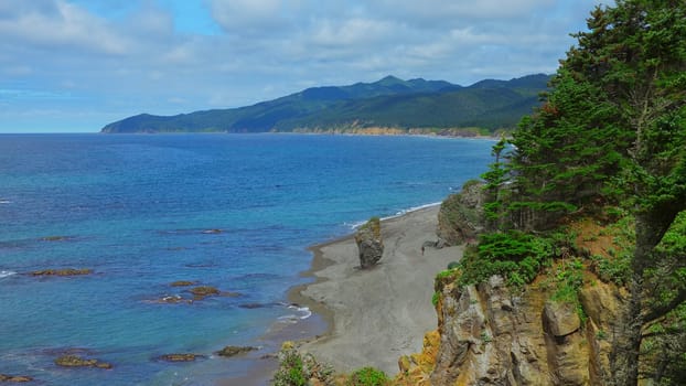 Beautiful view of bend of coast with rocks on sunny day. Clip. Landscape of rocky coast with green mountains and forest. Beautiful beach with rocks and blue sea on sunny day.