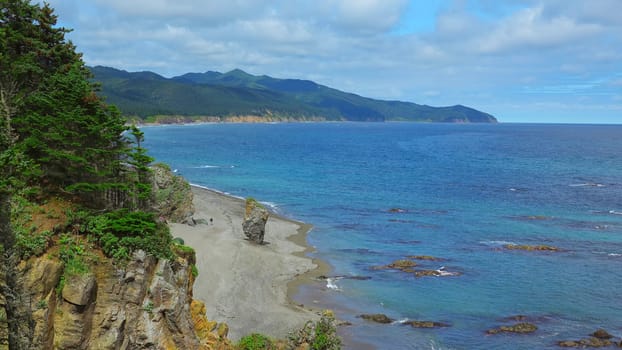 Beautiful view of bend of coast with rocks on sunny day. Clip. Landscape of rocky coast with green mountains and forest. Beautiful beach with rocks and blue sea on sunny day.