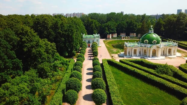 Top view of people walking on territory of palace garden. Creative. Beautiful road of palace garden with beautiful bushes and trees. Old building of royal estate with garden on sunny summer day.