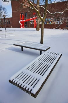 Peaceful winter scene in Fort Wayne, Indiana with fresh snow blanket on park bench, barren tree and vibrant public art