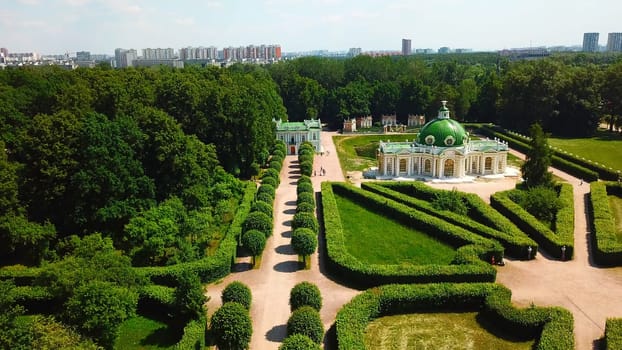 Top view of people walking on territory of palace garden. Creative. Beautiful road of palace garden with beautiful bushes and trees. Old building of royal estate with garden on sunny summer day.