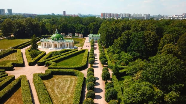 Top view of people walking on territory of palace garden. Creative. Beautiful road of palace garden with beautiful bushes and trees. Old building of royal estate with garden on sunny summer day.