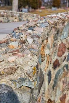 Detail of a rustic stone wall in Lindenwood Cemetery, Fort Wayne, showcasing natural textures and craftsmanship in a serene park setting.