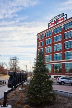 Modern red-brick Electric Works building under blue sky in Fort Wayne, Indiana, showcasing urban development, sustainability and green city landscaping