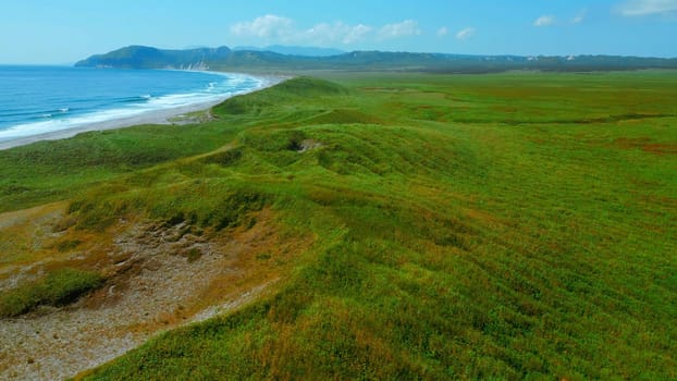 Aerial view of summer green meadows and mountains at the edge of the sea on the Isle of Skye, Scotland. Clip. Concept of summer nature