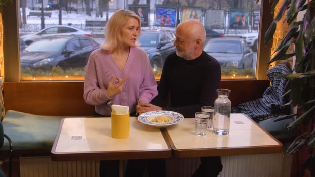 Beautiful elderly couple is chatting in cafe. Stock footage. Elderly couple is chatting sweetly on date in cafe. Beautiful couple on date in cozy cafe.