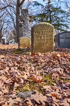 Vivid autumn leaves surround a weathered headstone in peaceful Lindenwood Cemetery, Fort Wayne, capturing the serene passage of time.