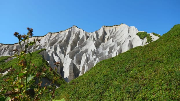 Amazing white mountains with green grass. Clip. Beautiful patterns on rocky white mountain with bright greenery on sunny summer day. White rocks of volcanic origin on island on summer day.