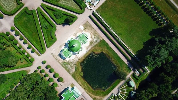 Top view of old estate with garden and pond. Creative. Beautiful garden area with patterns of paths and pond on sunny summer day. People walk in royal garden on estate.