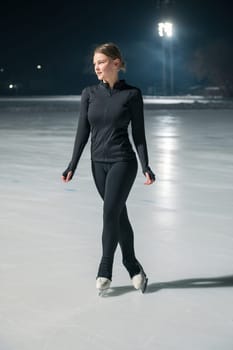 Beautiful young woman ice skating and performing she program over city outdoor ice arena. Winter activities concept