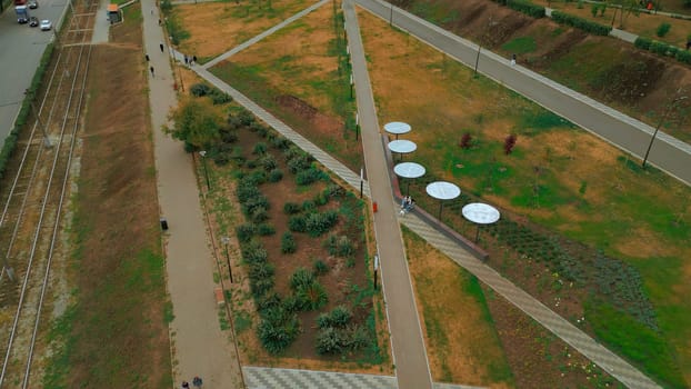 Top view of people walking in park alley in city. Clip. People walk and relax in modern city park. Landscape of city park alley with solar panels.