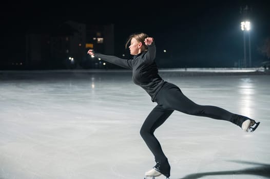 Beautiful young woman ice skating and performing she program over city outdoor ice arena. Winter activities concept