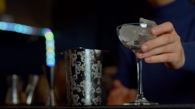 Close up bartender throwing away ice cubes from a small cocktail glass. Media. Cooling a glass for making a cocktail