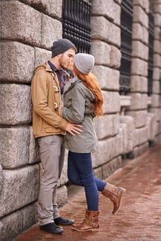 Couple, love and kiss with affection outdoor at sidewalk or against wall in cold weather, together and support in London. Relationship, date and bonding for romance with commitment, care and happy.