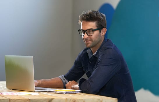 Smile, creative and man at laptop thinking for ideas, online research and reading email in office with glasses. Brainstorming, computer and designer at desk with business plan in professional career.