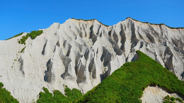 Amazing white mountains with green grass. Clip. Beautiful patterns on rocky white mountain with bright greenery on sunny summer day. White rocks of volcanic origin on island on summer day.