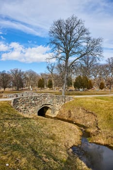 Serene Springtime in Fort Wayne - Historic Stone Bridge Over Stream Against Lindenwood Cemetery Backdrop