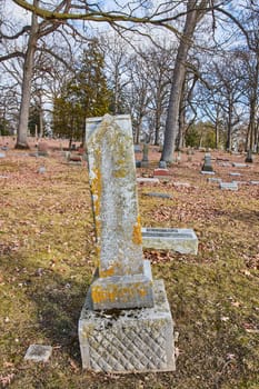 Time-weathered tombstone standing amid a serene graveyard in Lindenwood Cemetery, Fort Wayne, Indiana, under an overcast autumn sky