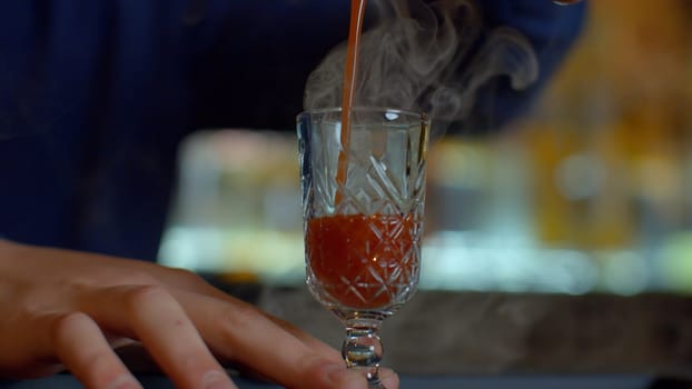 Close up of bartender at a bar counter pouring alcohol into vintage glass. Media. Pouring red hot alcoholic tincture with steam