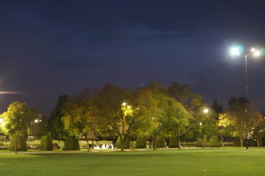 A park at night with a group of people sitting on benches. High quality photo