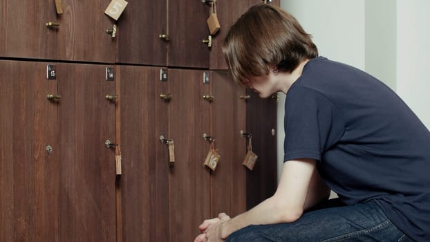 Young tired man sitting against a wooden gym cabinets. Media. Locker room in the gym