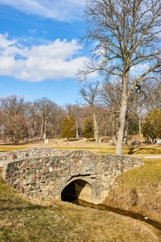 Stone bridge spanning a tranquil creek in Lindenwood Cemetery, Fort Wayne, Indiana. A picturesque scene of serenity and history in late fall.